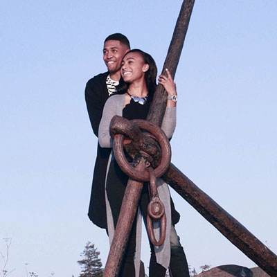 Alumni couple Craig & Tyler 16 pose together by a large boat anchor 