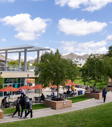 UCR campus: modern building, outdoor seating, green lawn, students, distant hills.