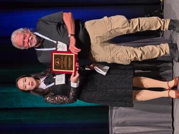 Yang Claire Yang and David Swanson stand next to each other, displaying the Mindel C. Sheps Award plaque that Swanson received.