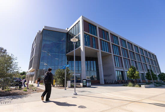 Modern university building with large windows, student walking on a sunny day.